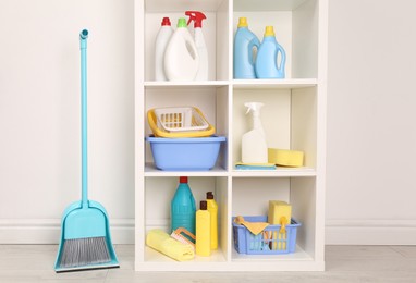 Photo of Shelving unit with detergents and cleaning tools near white wall indoors