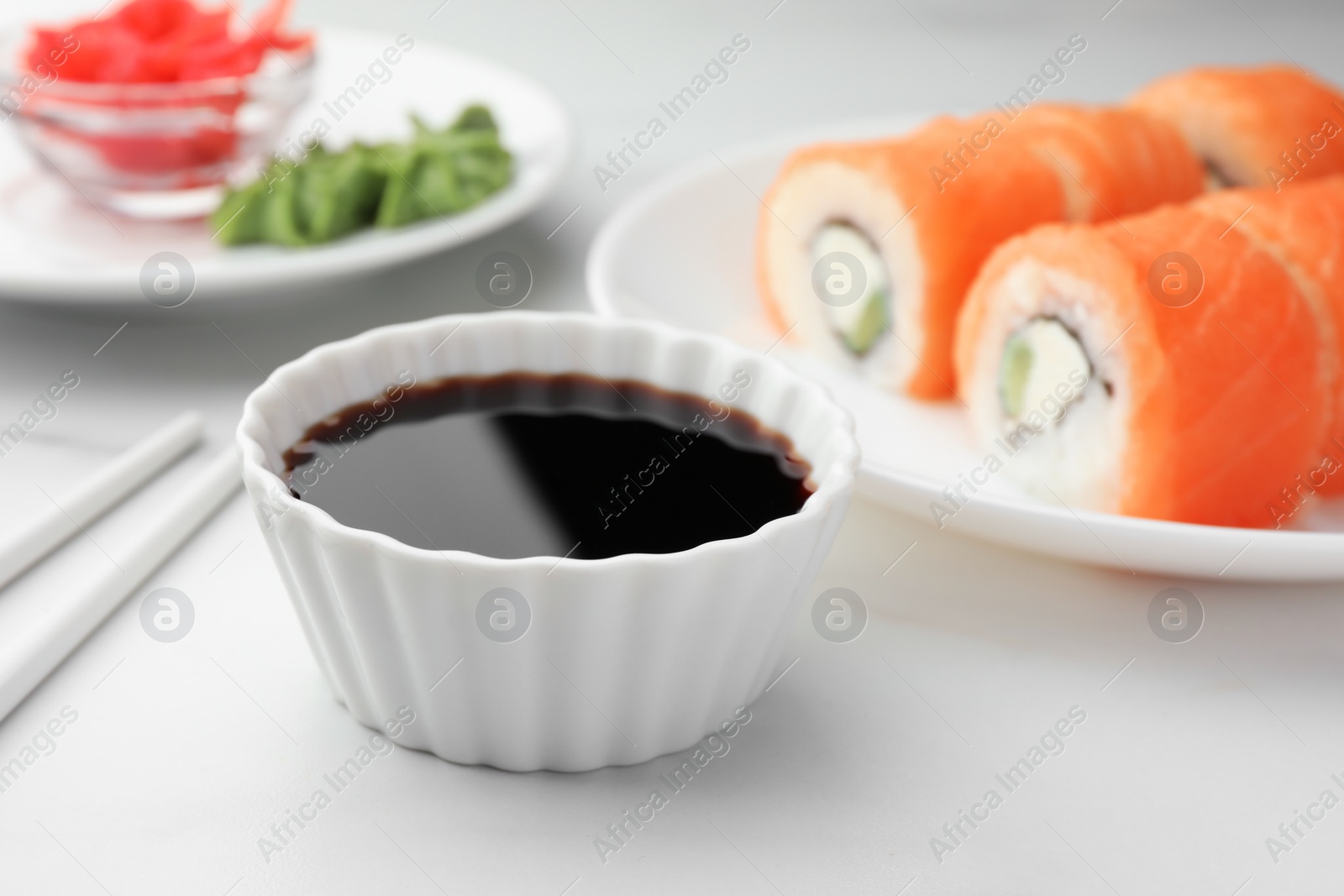 Photo of Tasty soy sauce in bowl and sushi on white marble table, closeup