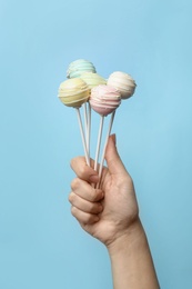 Woman holding sweet cake pops on light blue background, closeup