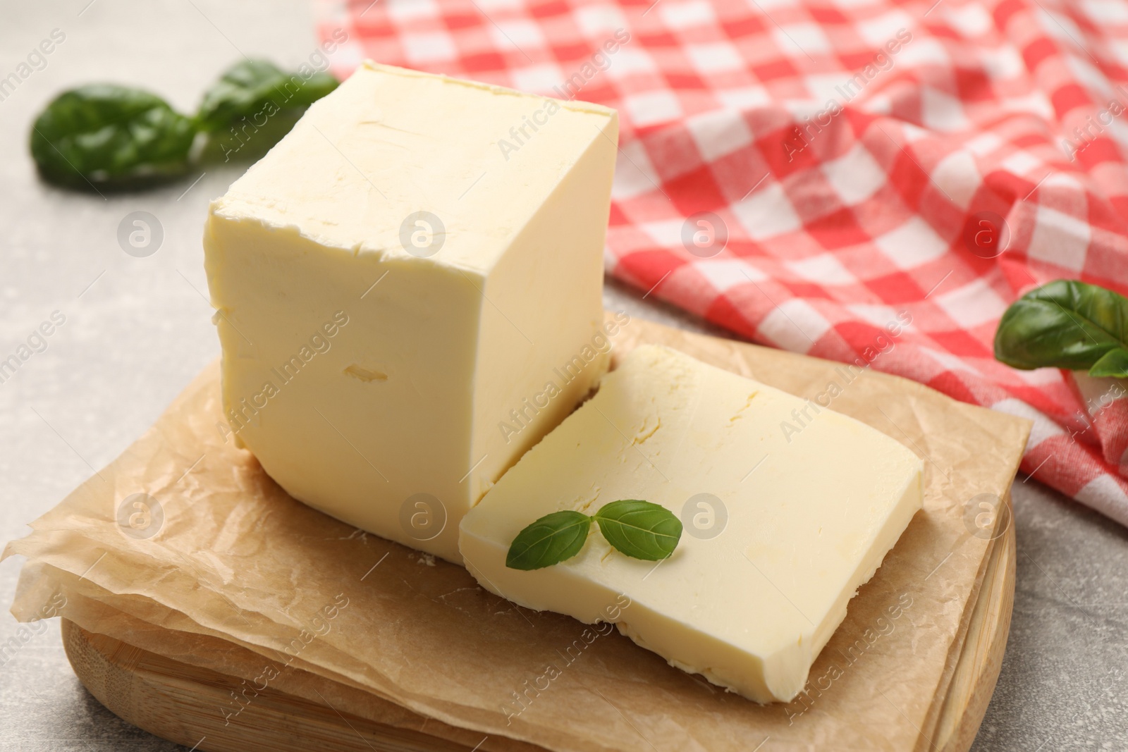 Photo of Block of tasty butter with basil on grey table, closeup