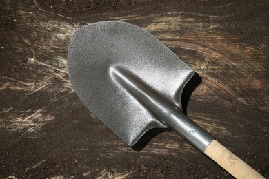 Photo of Metal shovel on dirty wooden surface, top view