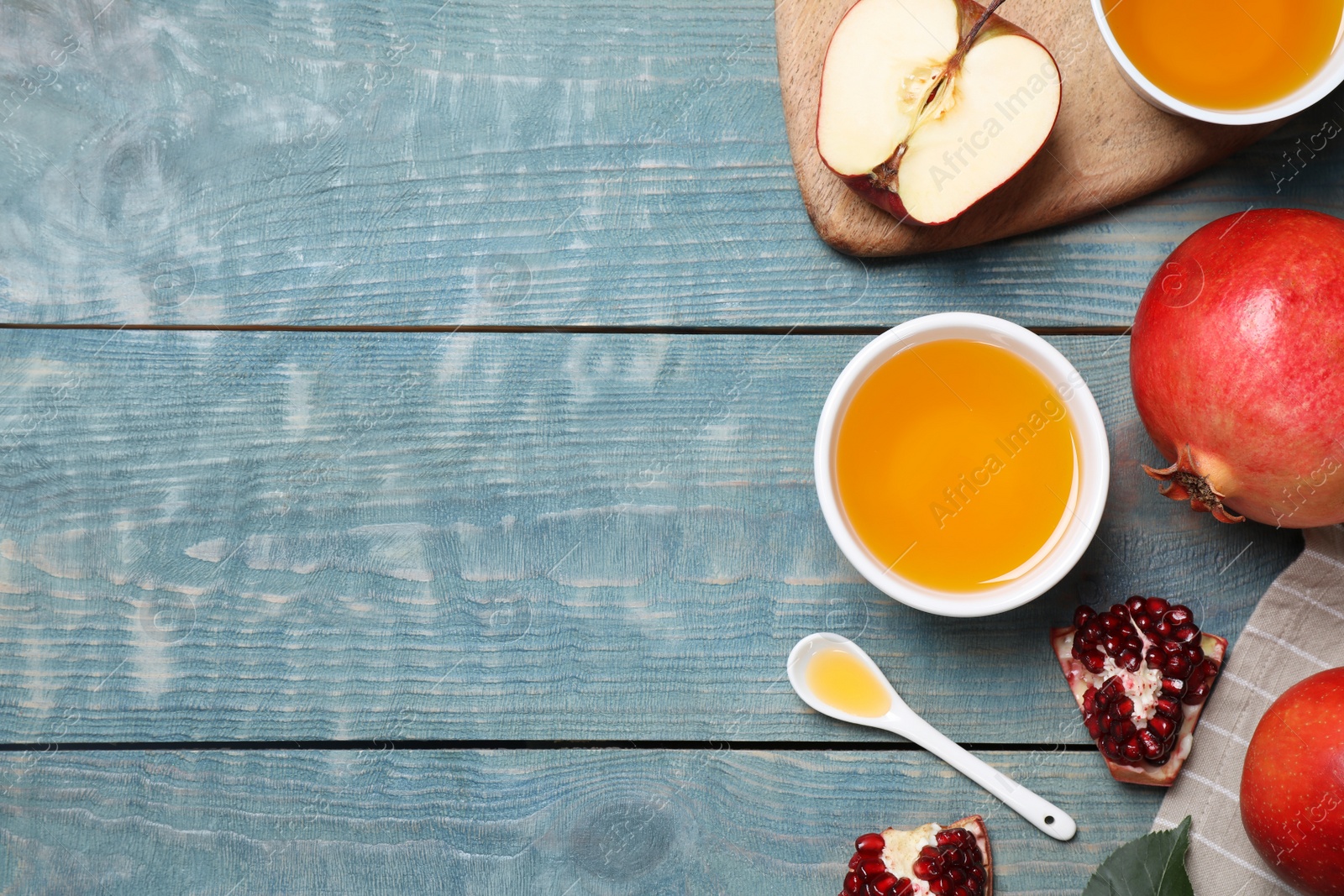 Photo of Honey, apples and pomegranates on blue wooden table, flat lay with space for text. Rosh Hashanah holiday