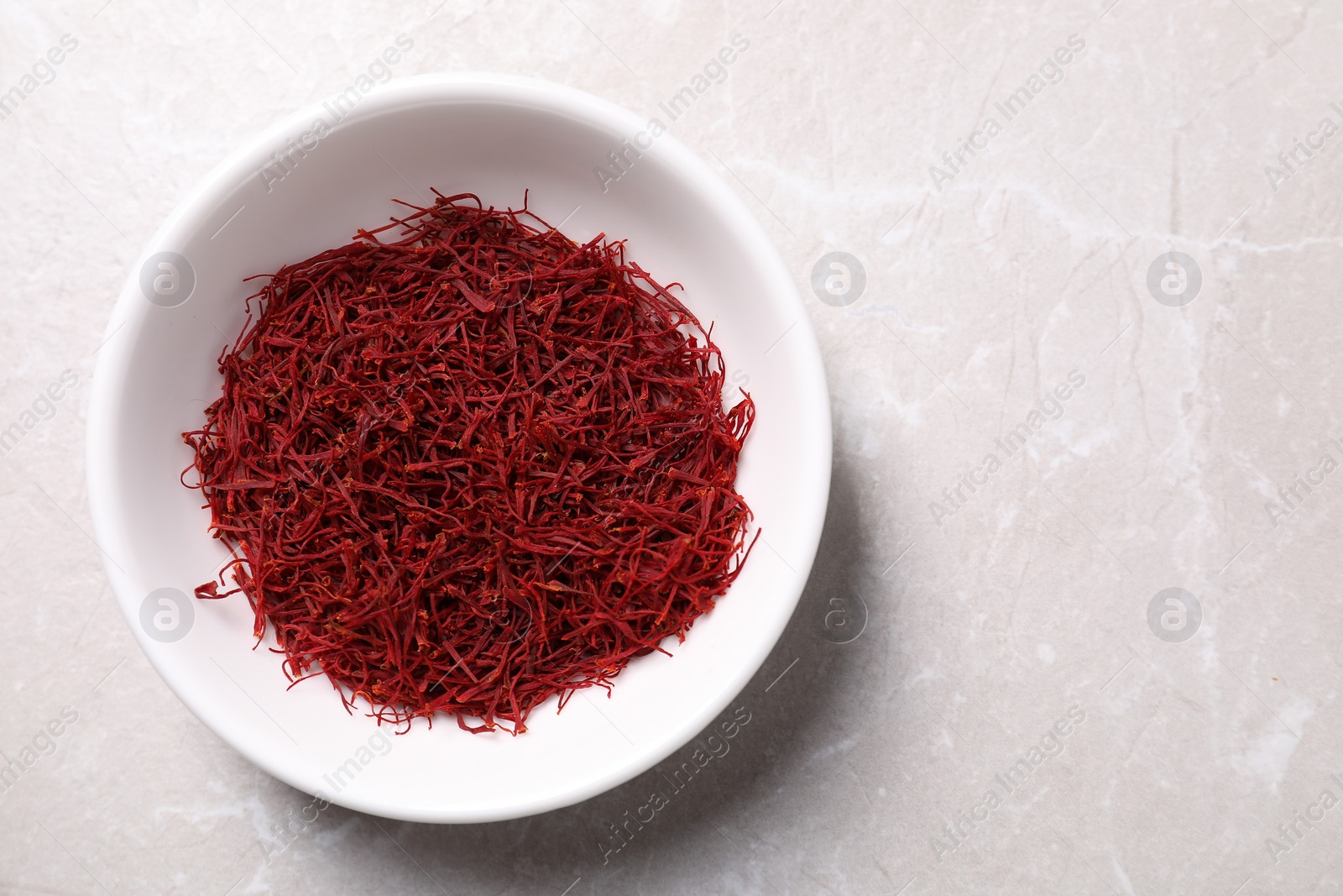 Photo of Aromatic saffron in bowl on light gray table, top view. Space for text