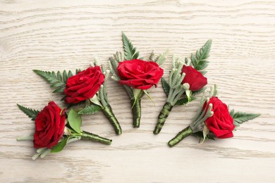 Many stylish red boutonnieres on light wooden table, flat lay