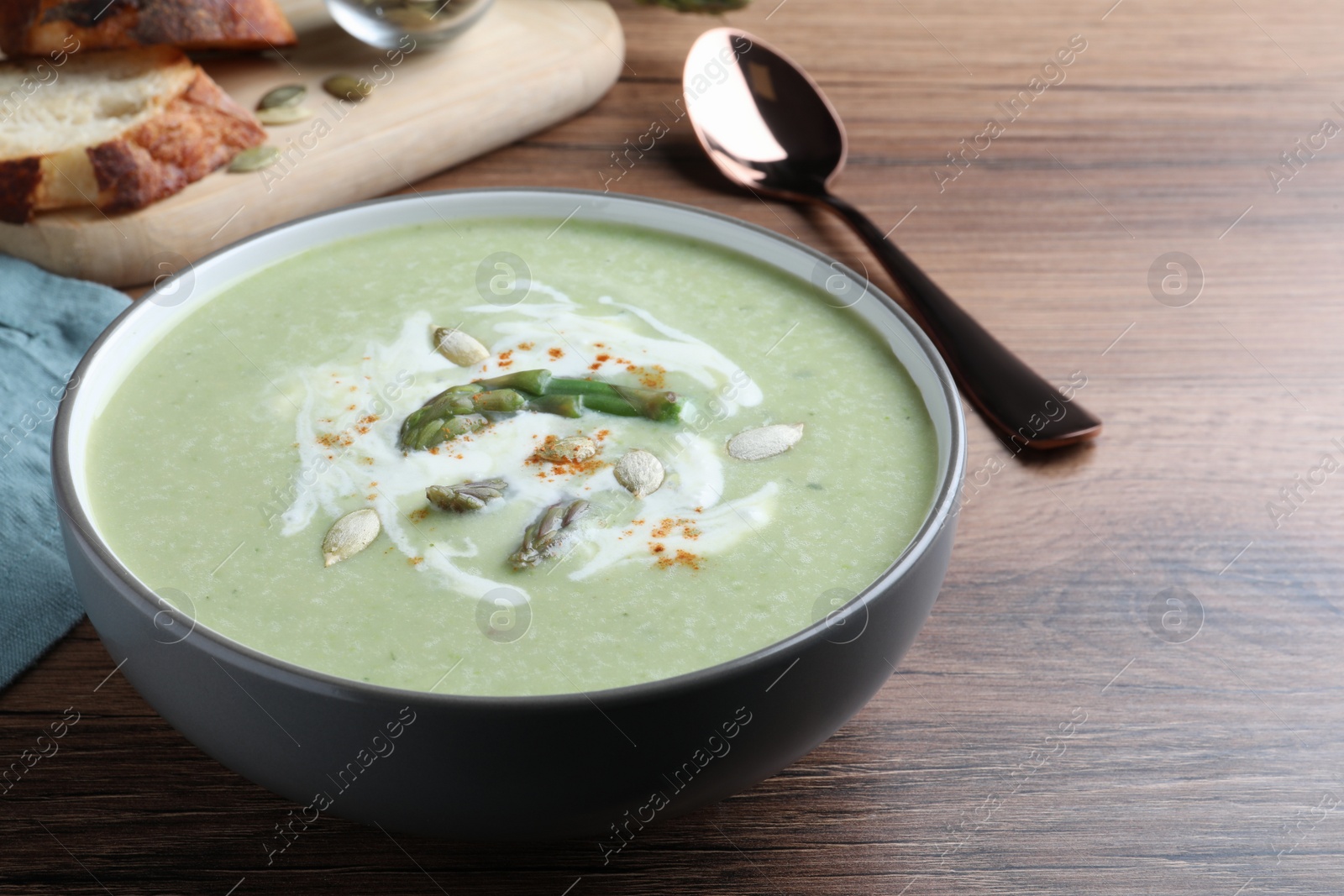 Photo of Delicious asparagus soup with pumpkin seeds served on wooden table, closeup