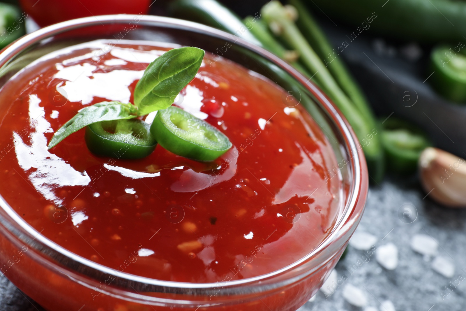 Photo of Spicy chili sauce in glass bowl on table, closeup