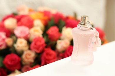 Bottle of perfume on white table against bouquet of beautiful roses. Space for text