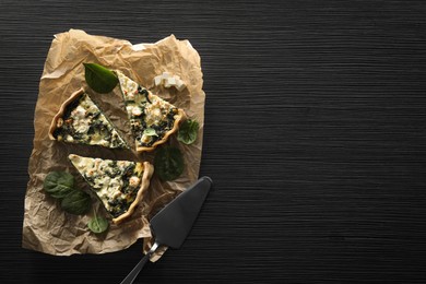 Delicious homemade spinach quiche on black wooden table, top view. Space for text