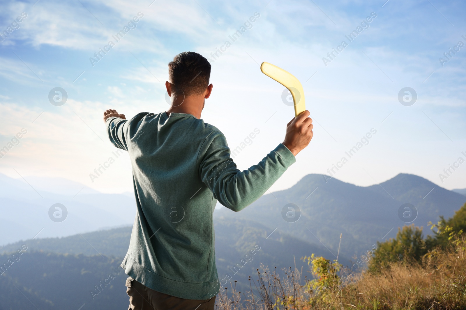 Photo of Man throwing boomerang in mountains on sunny day, back view