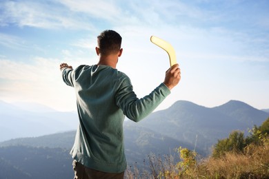 Photo of Man throwing boomerang in mountains on sunny day, back view