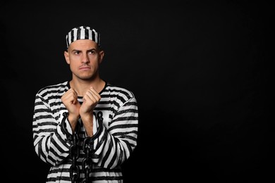 Prisoner in striped uniform with chained hands on black background, space for text