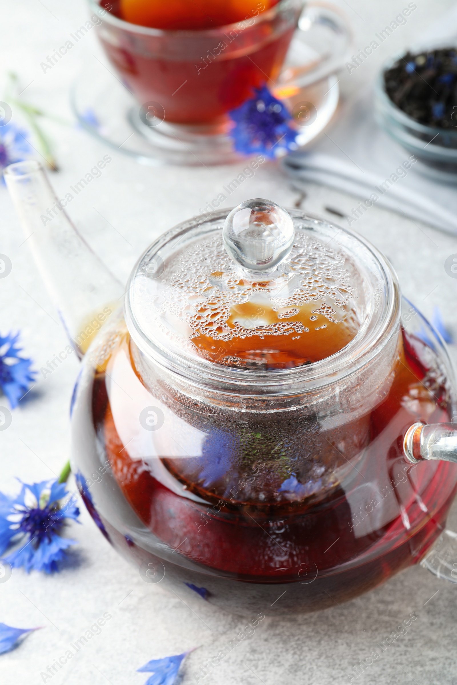 Photo of Glass pot with tea and cornflowers on light table, closeup