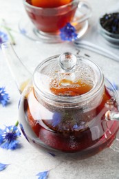 Glass pot with tea and cornflowers on light table, closeup