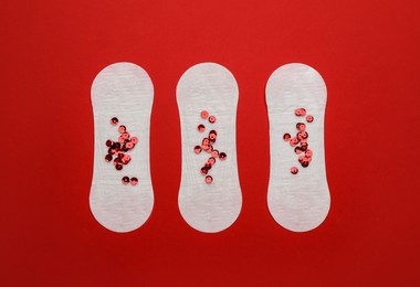 Photo of Sanitary pads with sequins on red background, flat lay. Menstrual cycle