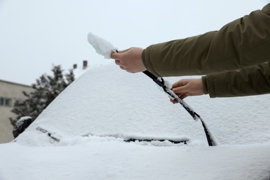 Photo of Woman cleaning wiper blade from snow outdoors, closeup
