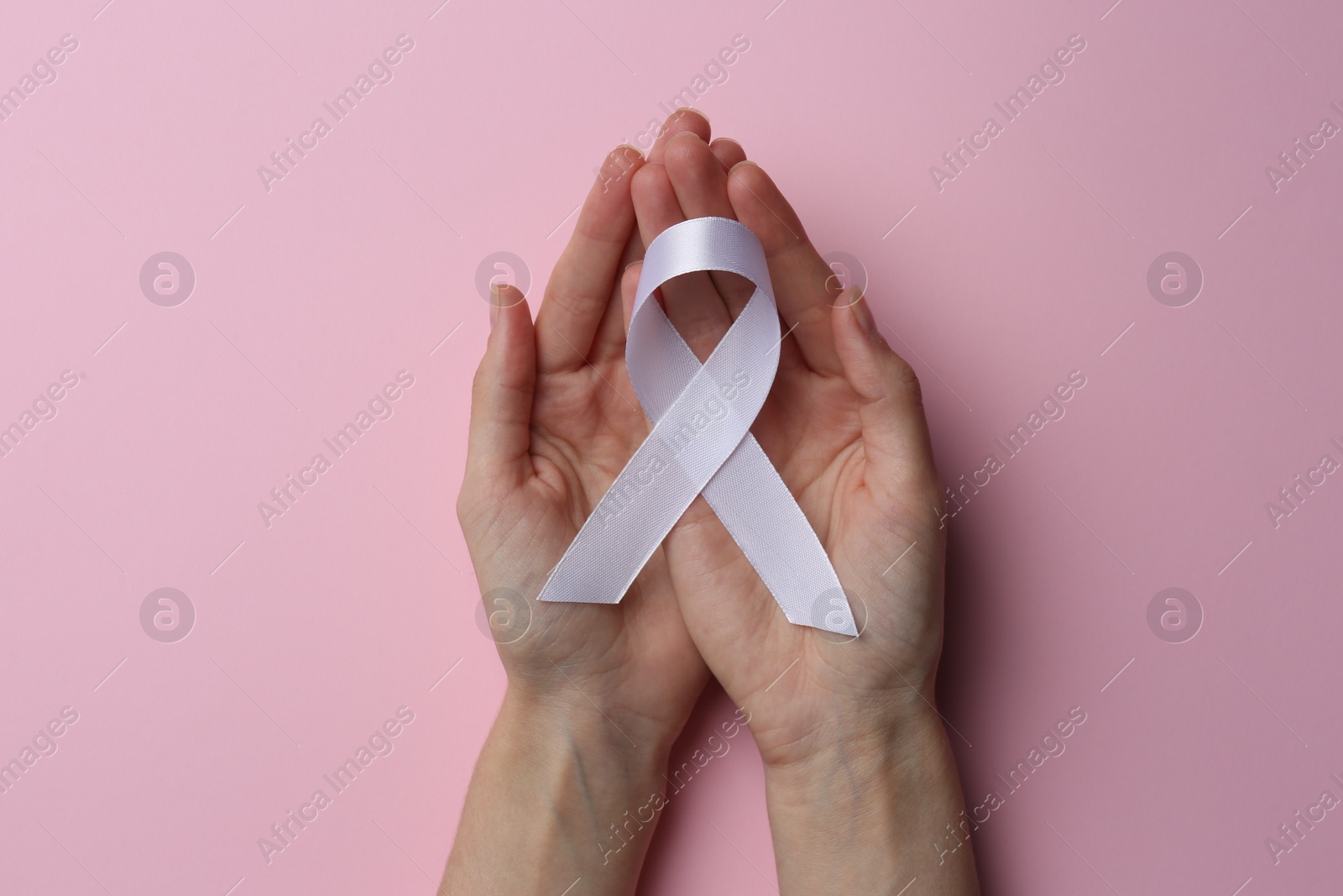 Photo of Woman holding white awareness ribbon on pink background, top view