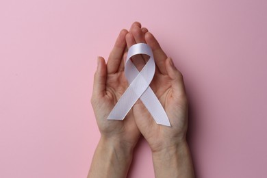 Photo of Woman holding white awareness ribbon on pink background, top view