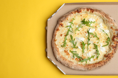 Photo of Delicious cheese pizza with arugula in takeout box on yellow background, top view. Space for text