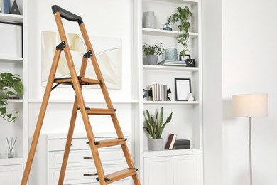 Photo of Wooden folding ladder near chest of drawers and shelves with accessories indoors