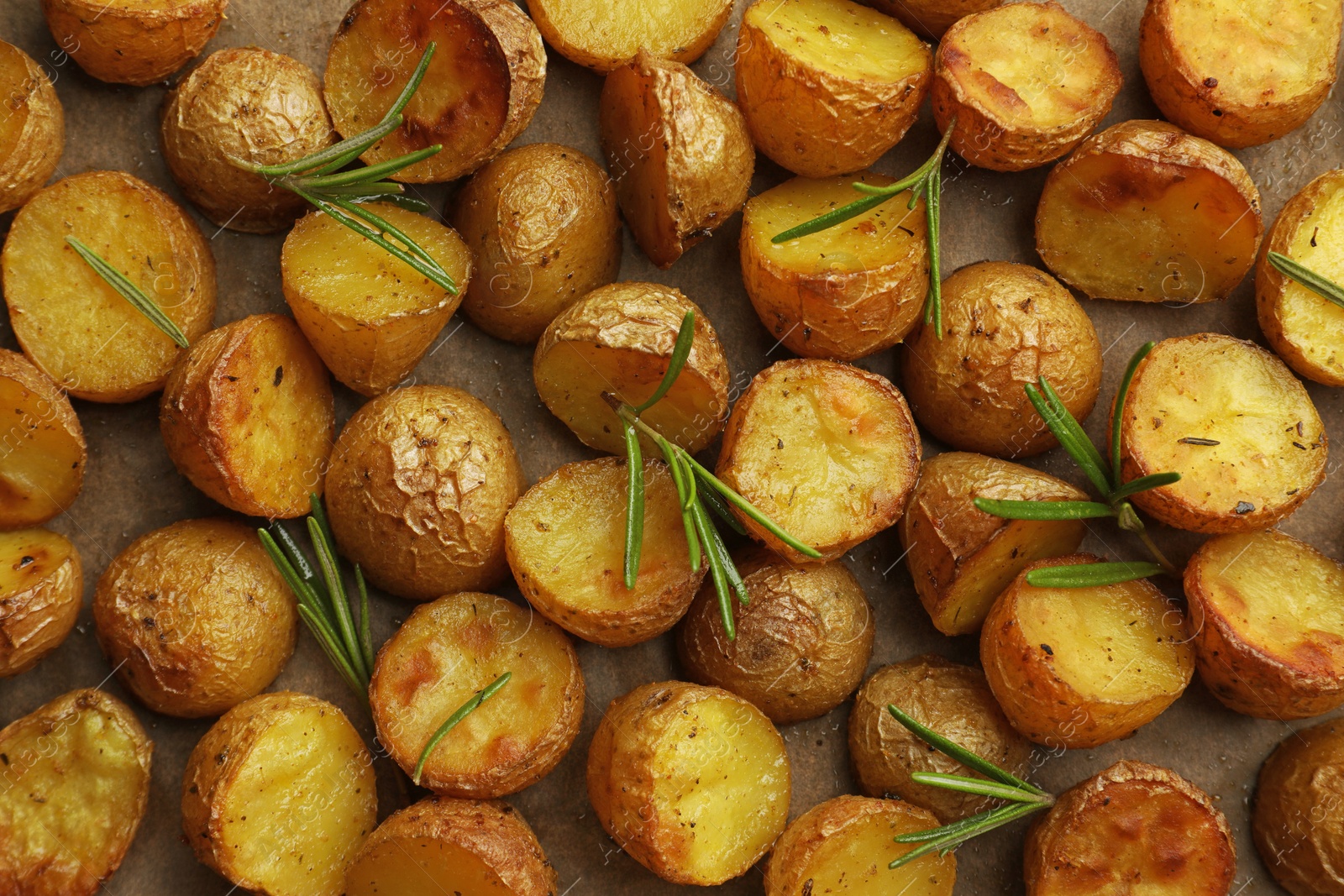 Photo of Tasty baked potato and aromatic rosemary on parchment paper, flat lay