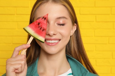 Photo of Beautiful girl with piece of watermelon near yellow brick wall, closeup