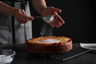 Photo of Woman decorating tasty apricot pie with powdered sugar at black table, closeup