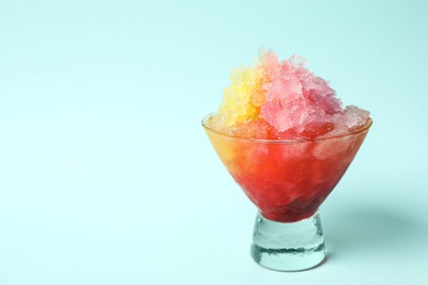 Rainbow shaving ice in glass dessert bowl on light blue background, closeup. Space for text