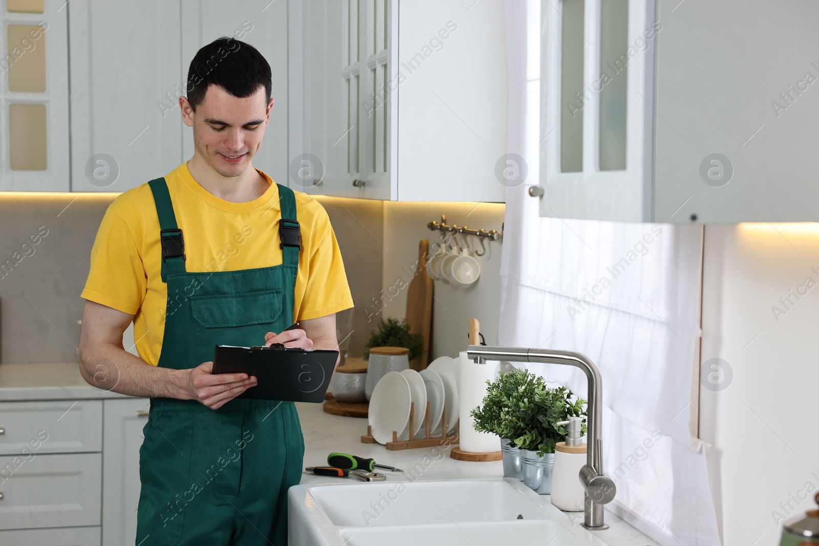 Photo of Smiling plumber with clipboard near faucet in kitchen