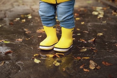 Photo of Little girl standing in puddle outdoors, closeup