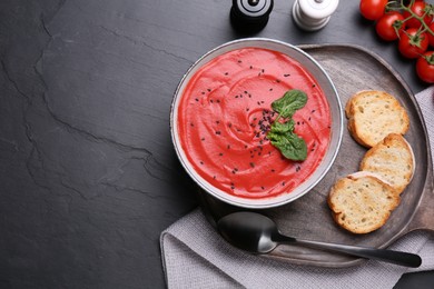 Photo of Delicious tomato cream soup with bread on black table, flat lay. Space for text