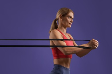 Photo of Athletic woman exercising with elastic resistance band on purple background
