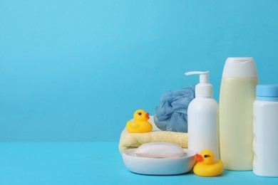 Photo of Baby cosmetic products, bath ducks, sponge and towel on light blue background. Space for text