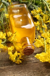 Photo of Rapeseed oil in glass bottle and beautiful yellow flowers on wooden table