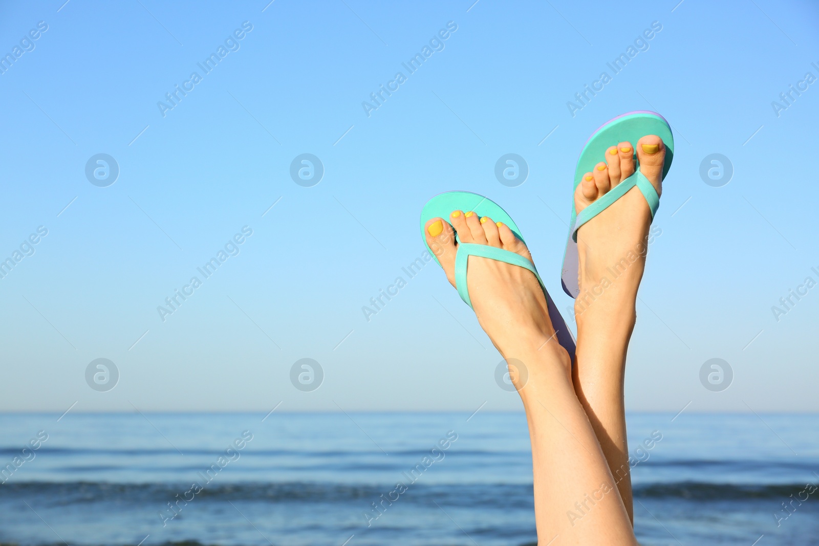 Photo of Closeup of woman wearing flip flops near sea, space for text. Beach accessories