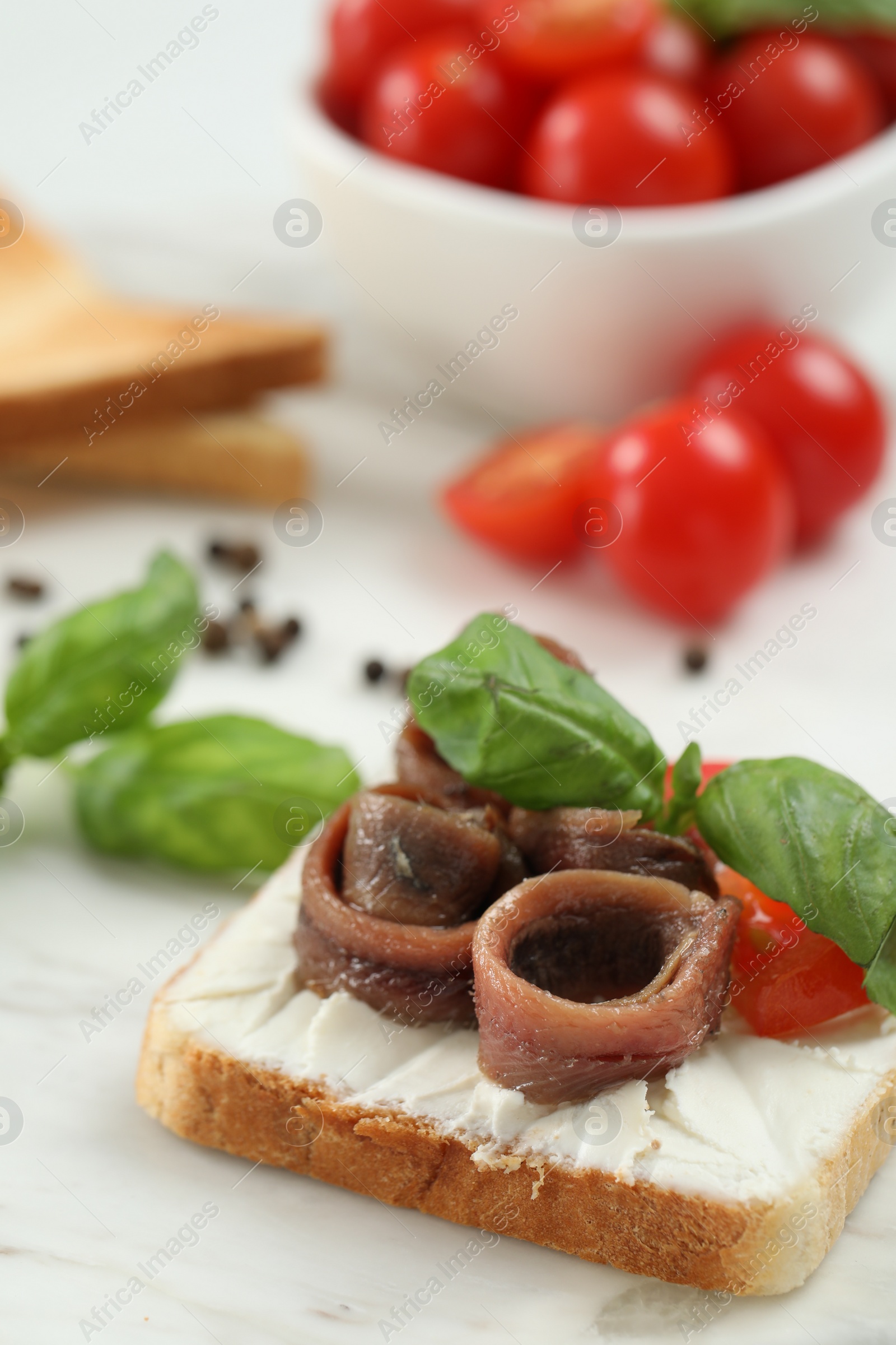 Photo of Delicious sandwich with cream cheese, anchovies and tomato on white marble table, closeup. Space for text