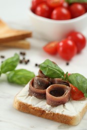 Delicious sandwich with cream cheese, anchovies and tomato on white marble table, closeup. Space for text