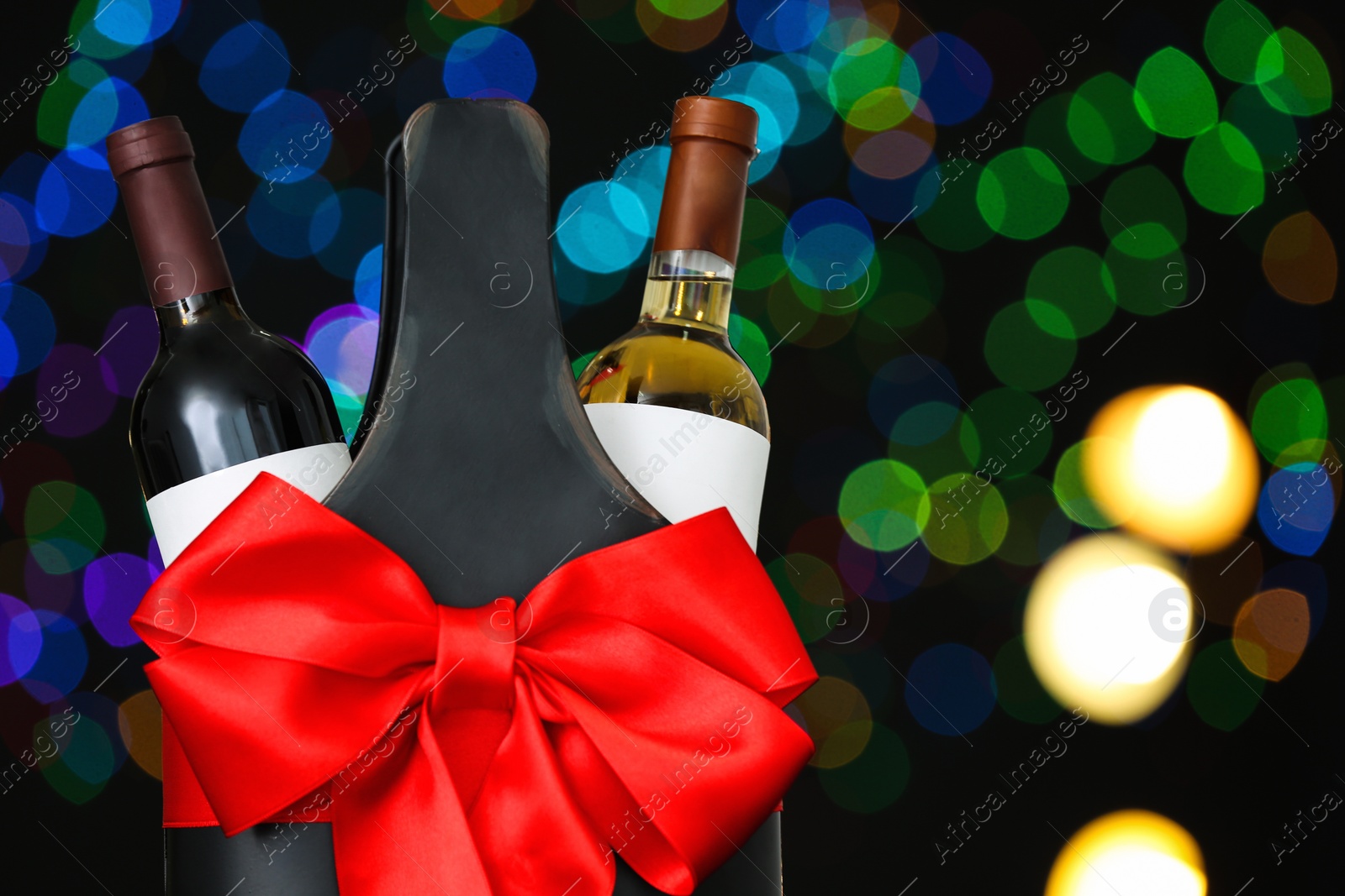 Photo of Festive package with bottles of wine against blurred lights, space for text. Bokeh effect