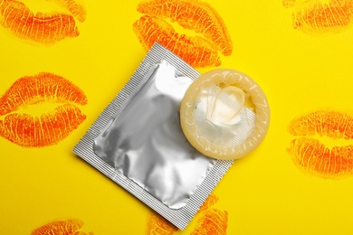 Photo of Condom with lipstick kiss marks on yellow background, flat lay. Safe sex