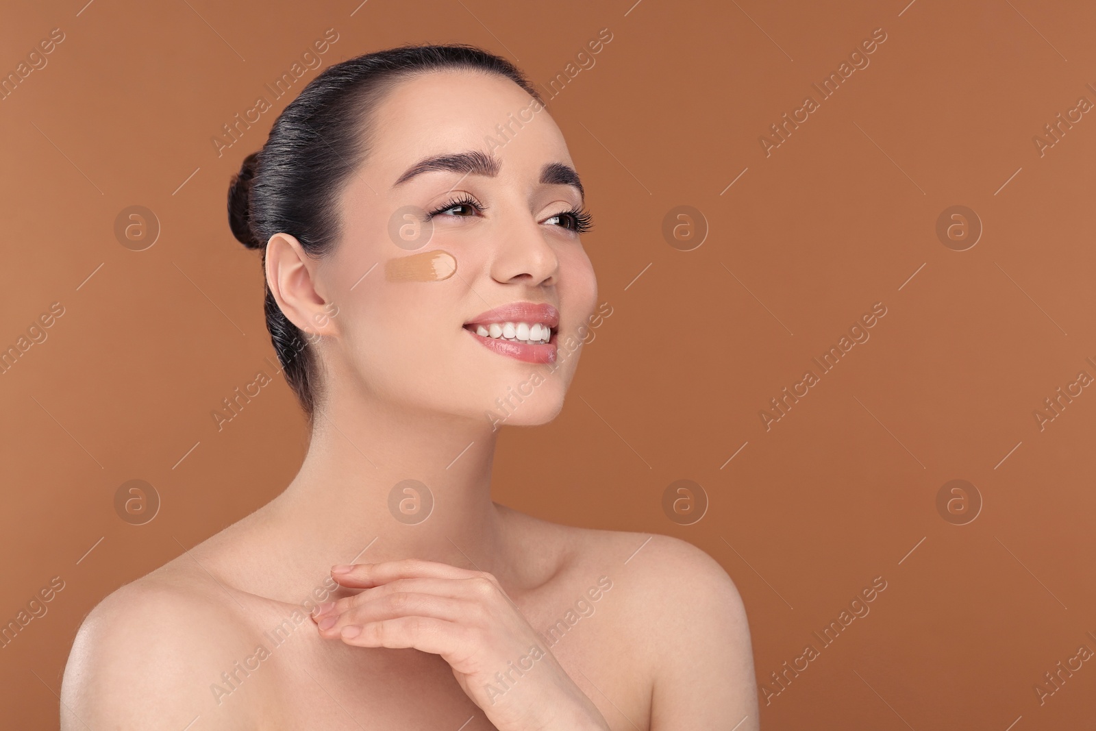 Photo of Woman with swatch of foundation on face against brown background. Space for text