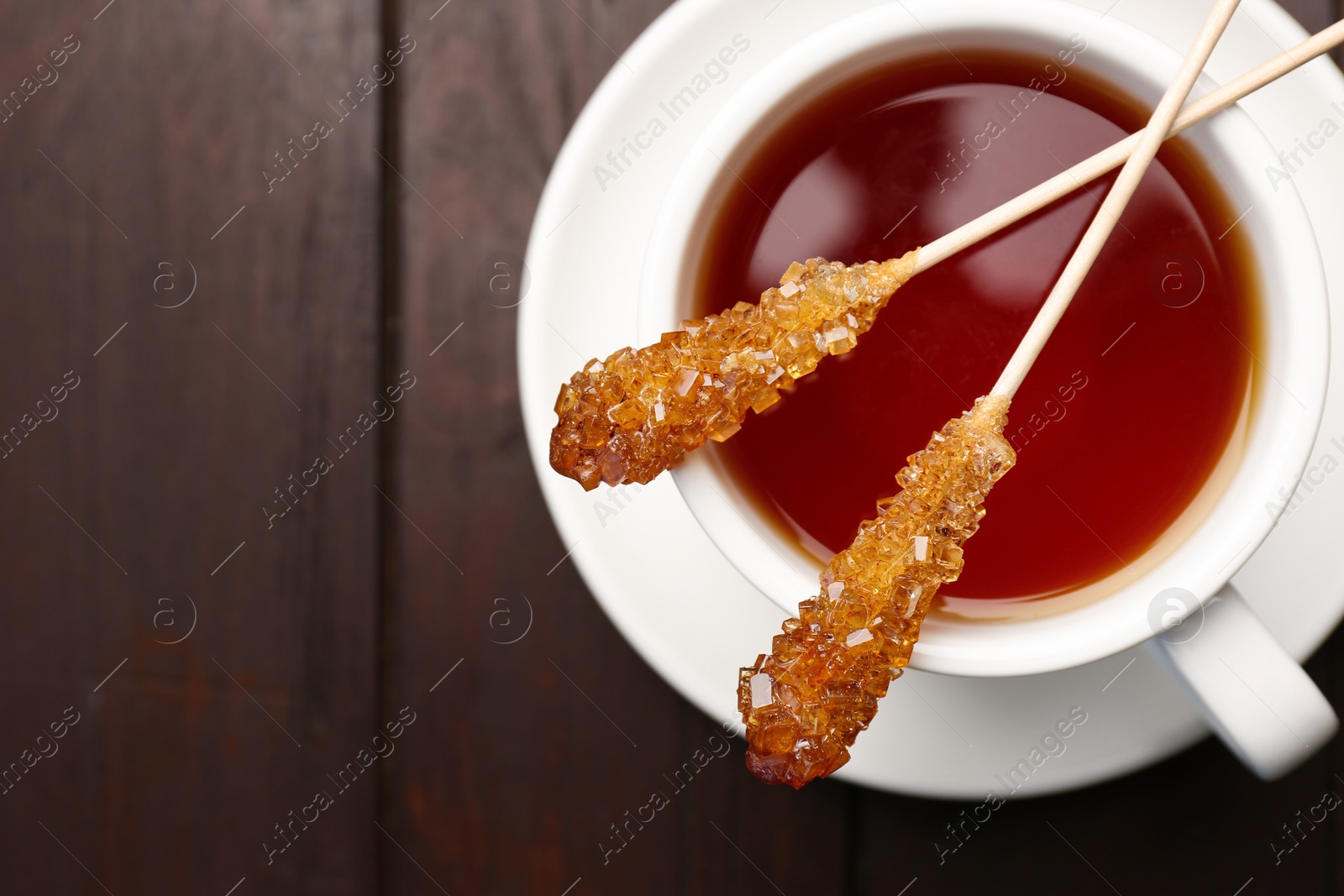 Photo of Sticks with sugar crystals and cup of tea on wooden table, top view. Space for text