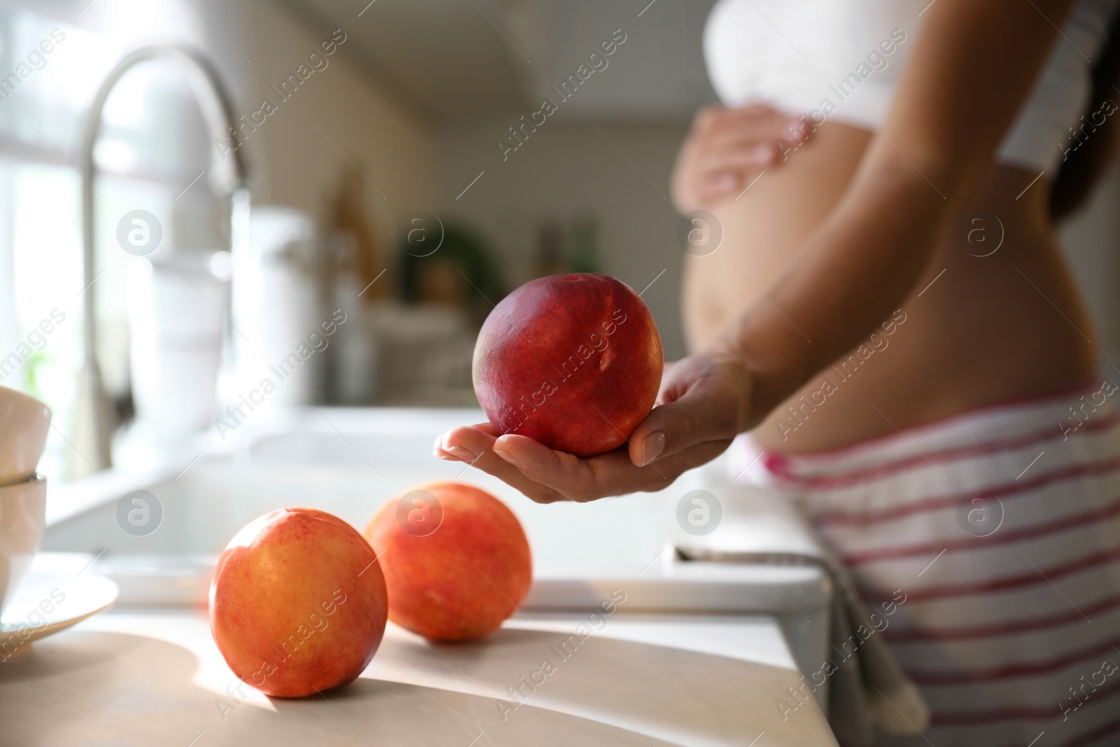 Photo of Young pregnant woman washing fresh sweet peaches in kitchen, closeup. Taking care of baby health