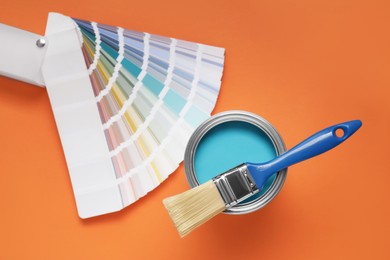 Photo of Can with light blue paint, brush and color palette on orange background, flat lay