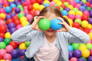 Photo of Happy little girl holding colorful balls in ball pit