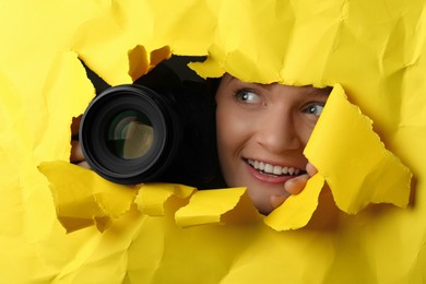 Photo of Hidden woman with camera spying through hole in yellow paper