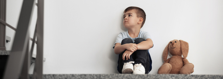 Image of Sad little boy sitting near white wall, banner design with space for text. Time to visit child psychologist
