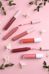 Different lip glosses, applicators, flowers and green leaves on pink background, flat lay