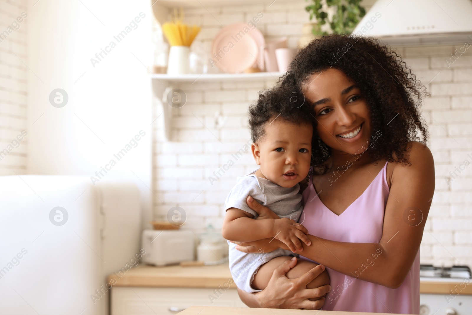 Photo of African-American woman with her baby in kitchen. Happiness of motherhood