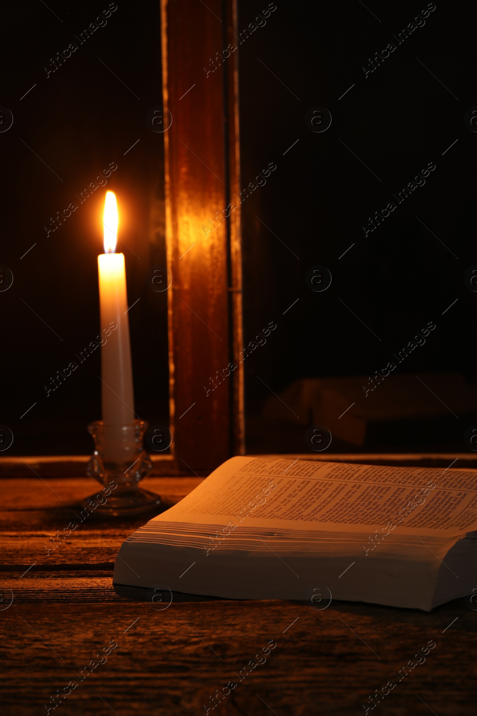 Photo of Burning candle and Bible on wooden table near window at night