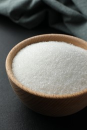 Photo of Granulated sugar in bowl on black table, closeup