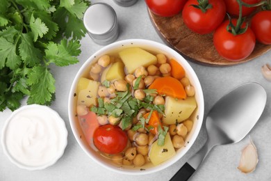 Photo of Flat lay composition of tasty chickpea soup in bowl, vegetables, sauce and spices served on light grey table